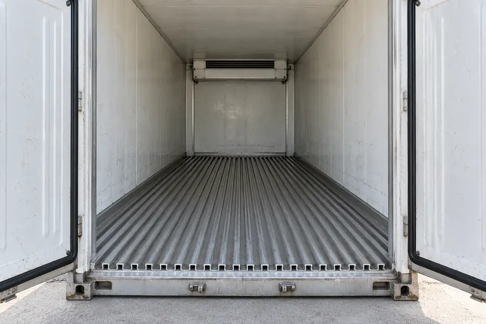 Ilustración del interior de un reefer usado de 20 pies con puertas abiertas, empaques y canales metálicos del piso visibles